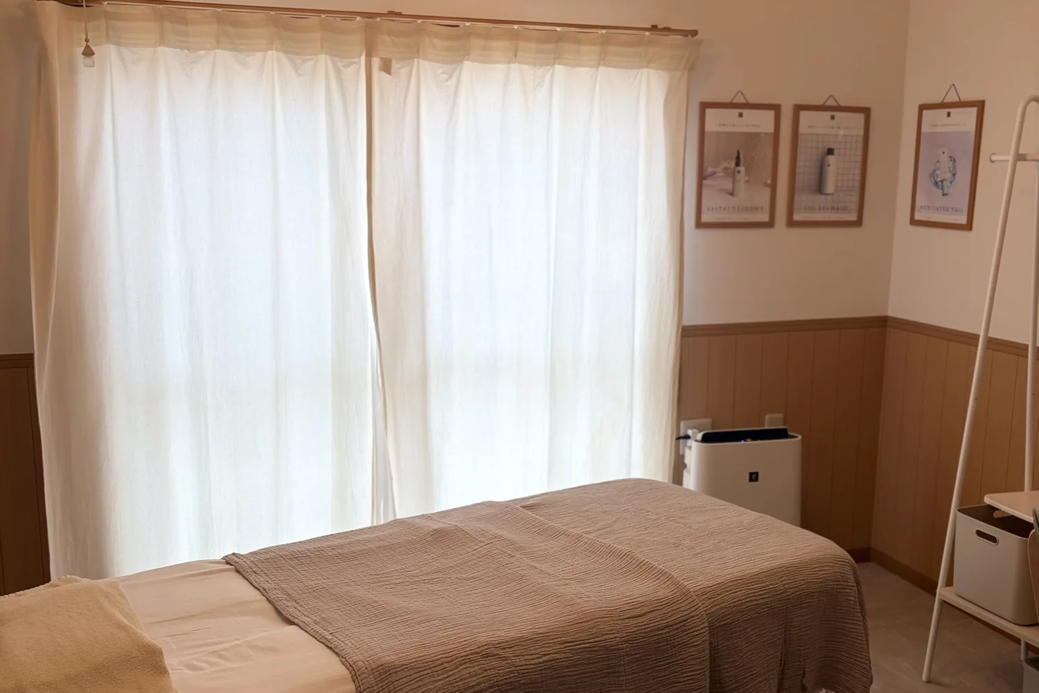 やわらかな光が入る施術ルーム。ベージュのブランケットを掛けた施術ベッド